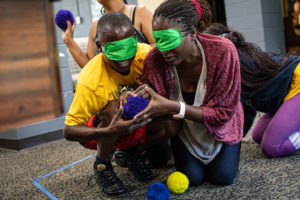 Blindfolded Fellows participate in a Common Leadership Curriculum team-building exercise during their Mandela Washington Fellowship Leadership Institute. They are kneeling on the ground touching different materials, including colorful fluffy balls.
