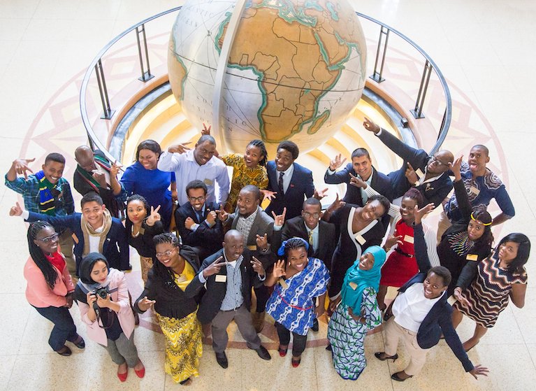 Fellows smile for a group photo in front of a map of Africa.