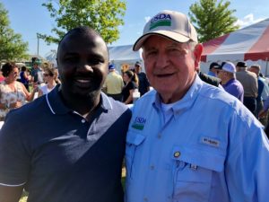 2019 Fellow Laurent Shilingi poses with Sonny Perdue, Secretary of Agriculture, at FarmFest during his PDE in Minnesota.