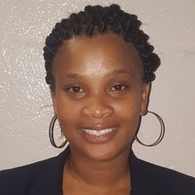 Headshot of a smiling woman with braided locs in a bun, black blazer, and hoop earrings