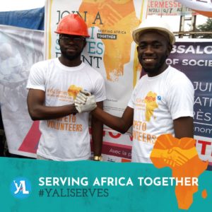 Two volunteers in hard hats shake hands. Accompanied by the text "Serving Africa Together #YALIServes"