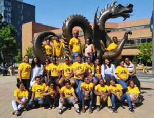 2019 Fellows pose in front of the dragon mascot at Drexel University. They are all wearing matching yellow Drexel t-shirts.
