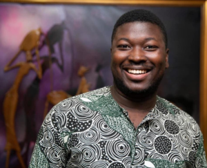 Fellowship Alumnus Laud Anthony Basing smiles while posing for a photo in front of a brown and purple background