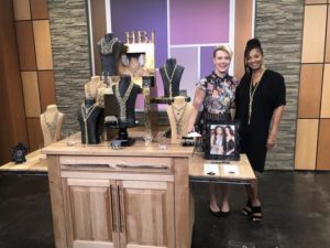 Two women stand behind a jewelry display on a television show set.