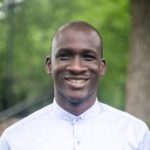 Man in a white shirt smiles for the camera outdoors