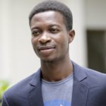 Headshot of a man in a NASA t-shirt and navy suit jacket; he looks off-camera