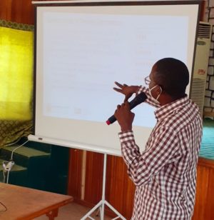 Man presents to a room, standing in front of a projection on a screen