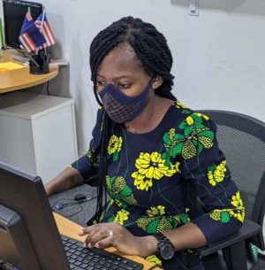 Woman sits at a computer; she is wearing a face mask