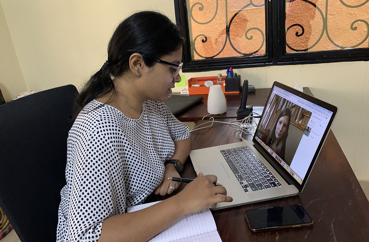 A woman sits at a laptop, engaged on a video call with another woman.
