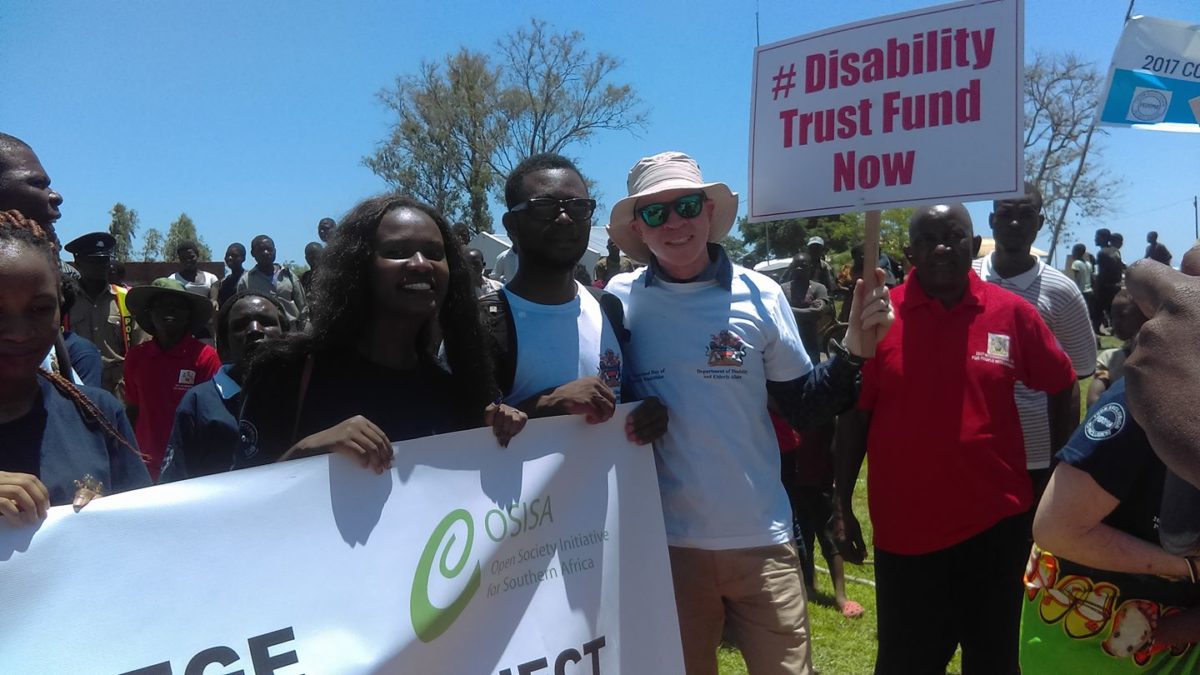 People at a disability rights rally. One holds a sign that says #DisabilityTrustFundNow