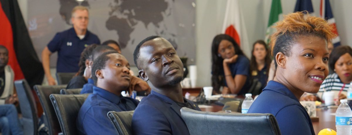 A group of Fellows sits at a table, faces turned toward a speaker, who is off-camera