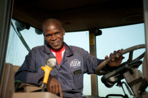 A man smiles, sitting in the driver's seat of a piece of farm equipment
