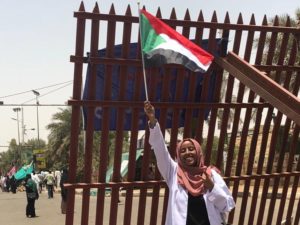 A woman in a medical coat waves a Sudanese flag high in the air