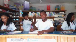 4 people stand behind the counter of a pharmacy, in various stages of work, smiling at the camera