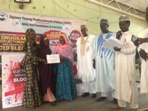 A group of people stand in front of a sign; some hold certificates