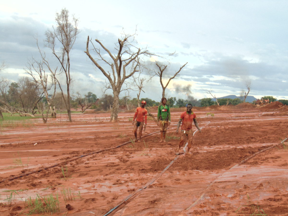 3 young men walk through a large patch of sandy red dirt
