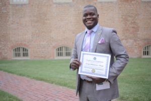 A man in a suit smiles and holds a certificate