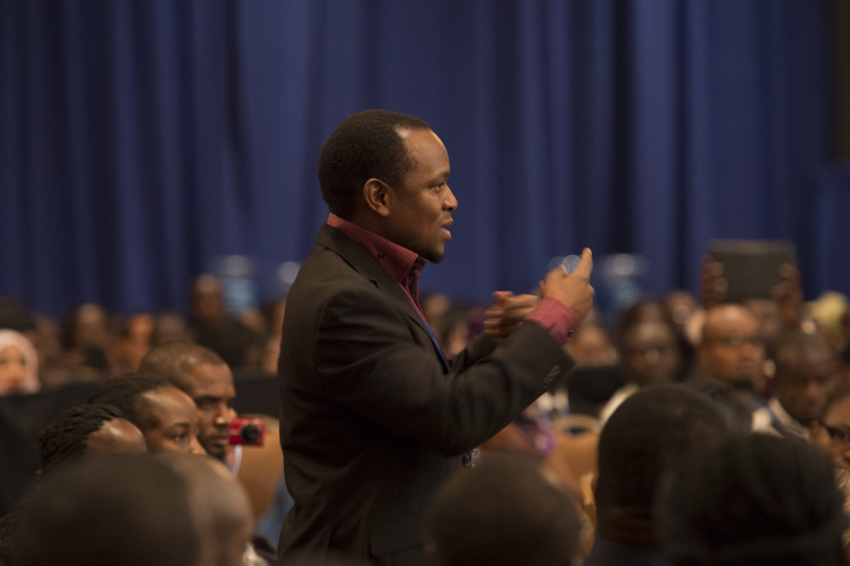 A man stands in a crowd and uses sign language.