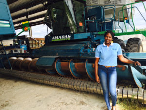 A woman stands in front of a piece of farm equipment in a barn.