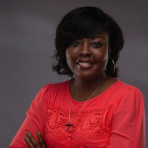 Woman in red blouse and hoop earrings with a cross necklace smiles at the camera