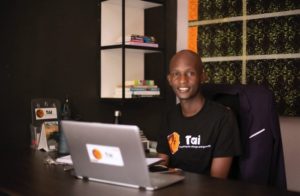 Man sits behind a desk; his clothing and equipment features the Tai Tanzania logo