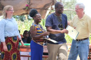 A man hands a certificate to workshop participants with other observes smiling and looking on