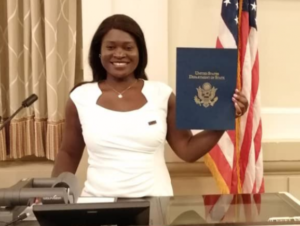 Smiling woman in a white dress holds up a certificate while standing at a podium