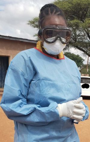 A woman in full personal protective equipment, including a mask, goggles, gloves, and a surgical gown