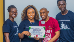 Woman presents certificate to participant; both smile for camera and are joined by 2 other colleagues