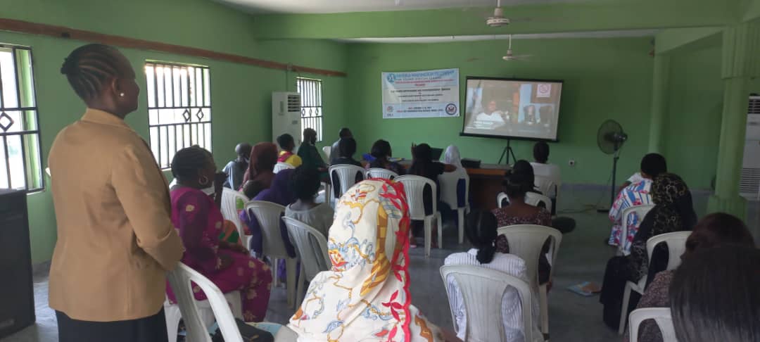 A group of deaf women look at a projector screen that has a video of a woman on it.