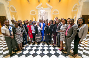 A group of people gathers for a posed photo in a large hall, painted yellow with a black and white checkered floor