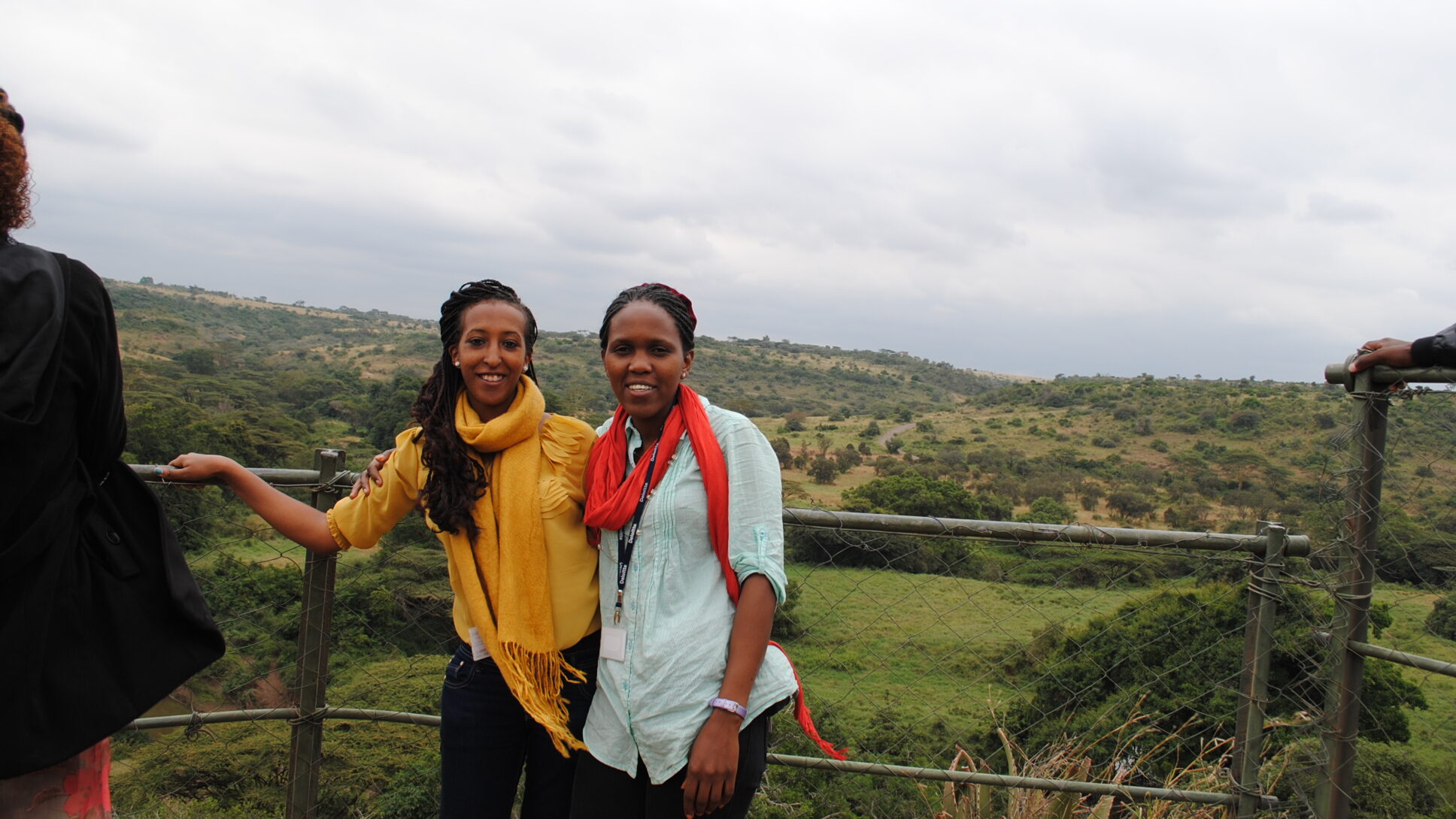 Two women pose in front a national park with trees and hills.