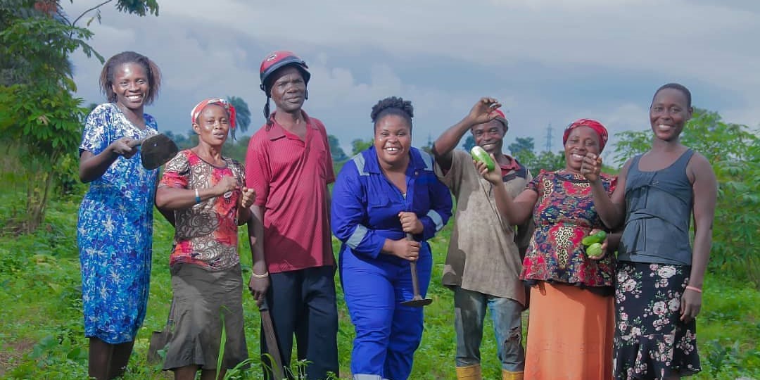 A group of farmers stand in a field holding produce