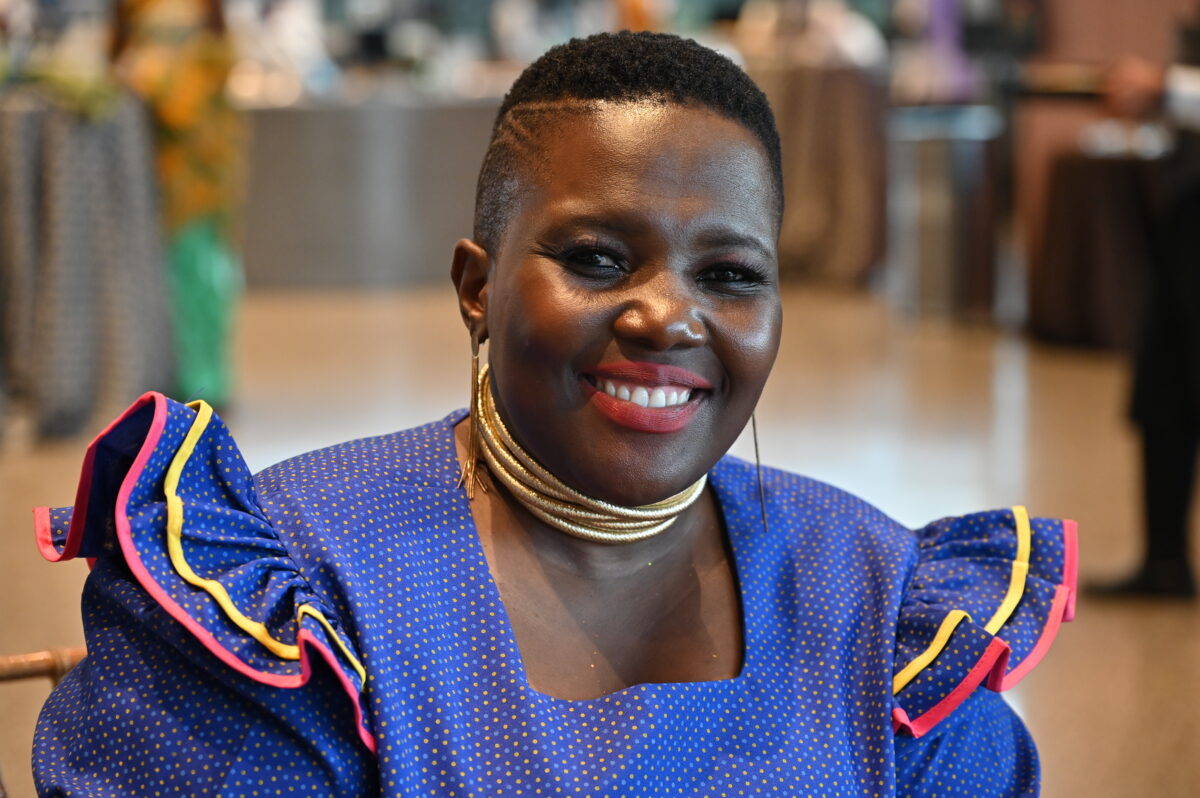 Photo of a young woman with short hair, a gold choker necklace, and blue blouse with ruffles