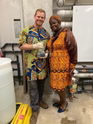 A man and woman in traditional Ivorian dress pose for a photo; the man holds a beaker filled with water