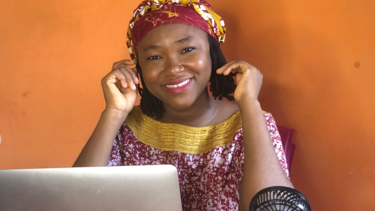 Woman in traditional dress sits behind a laptop and smiles at camera