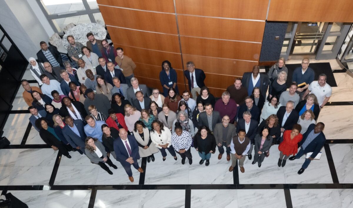 Large group of people standing in an atrium, looking up at the camera