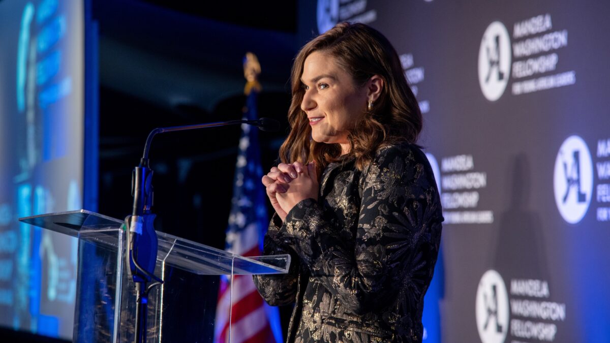 A woman speaks at a podium, clasping her hands as she makes remarks