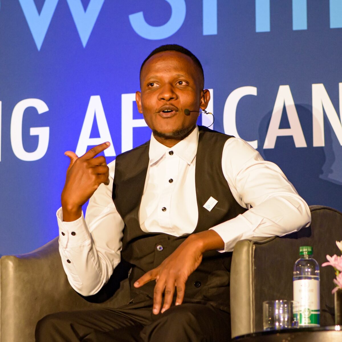 Candid photo of a man in business formal dress speaking on stage, seated in a chair