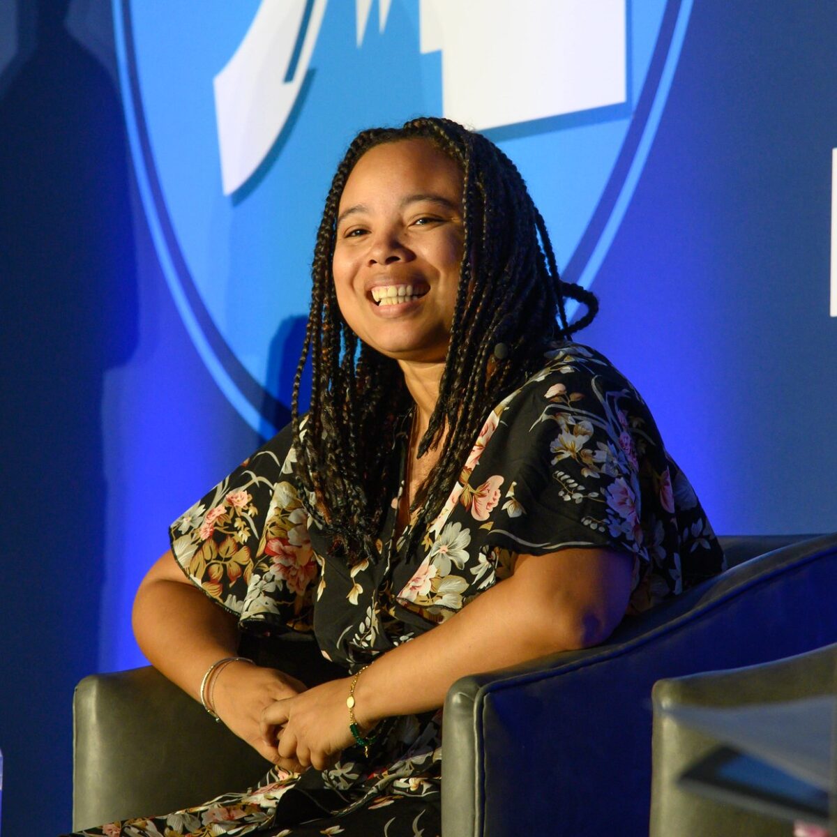 Candid photo of a woman with long locs sitting in a chair on a stage, smiling