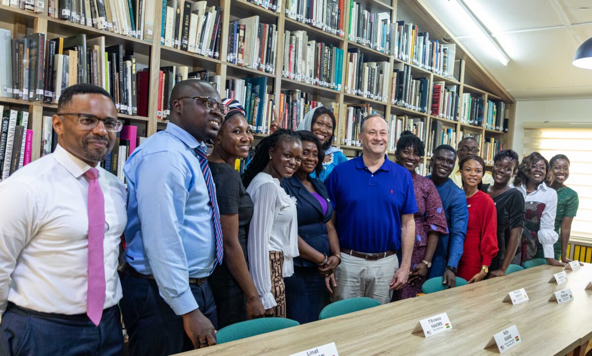 A group of about 12 people smile for a photo in front of a large bookcase