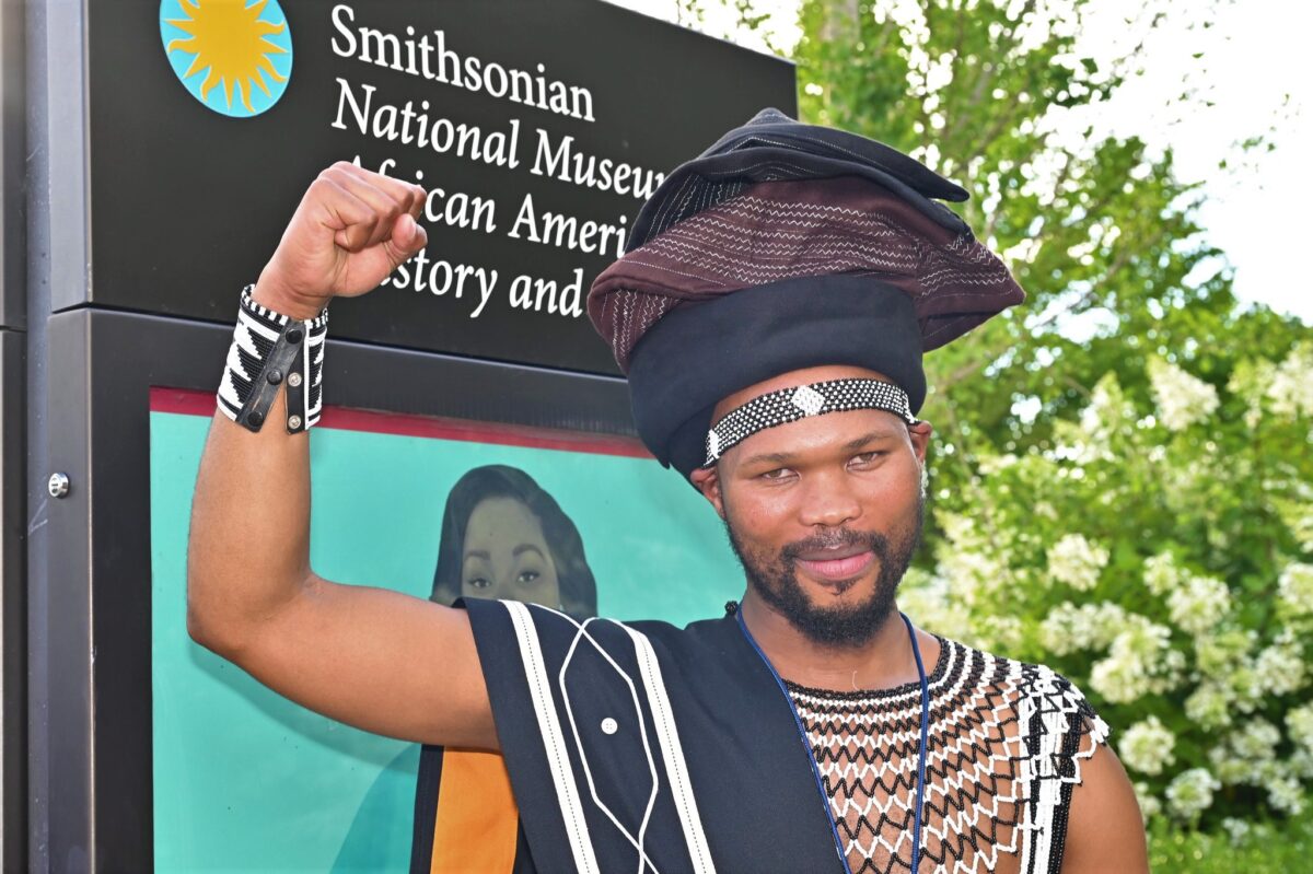 Man in traditional tribal dress holds his arm up in the strong pose