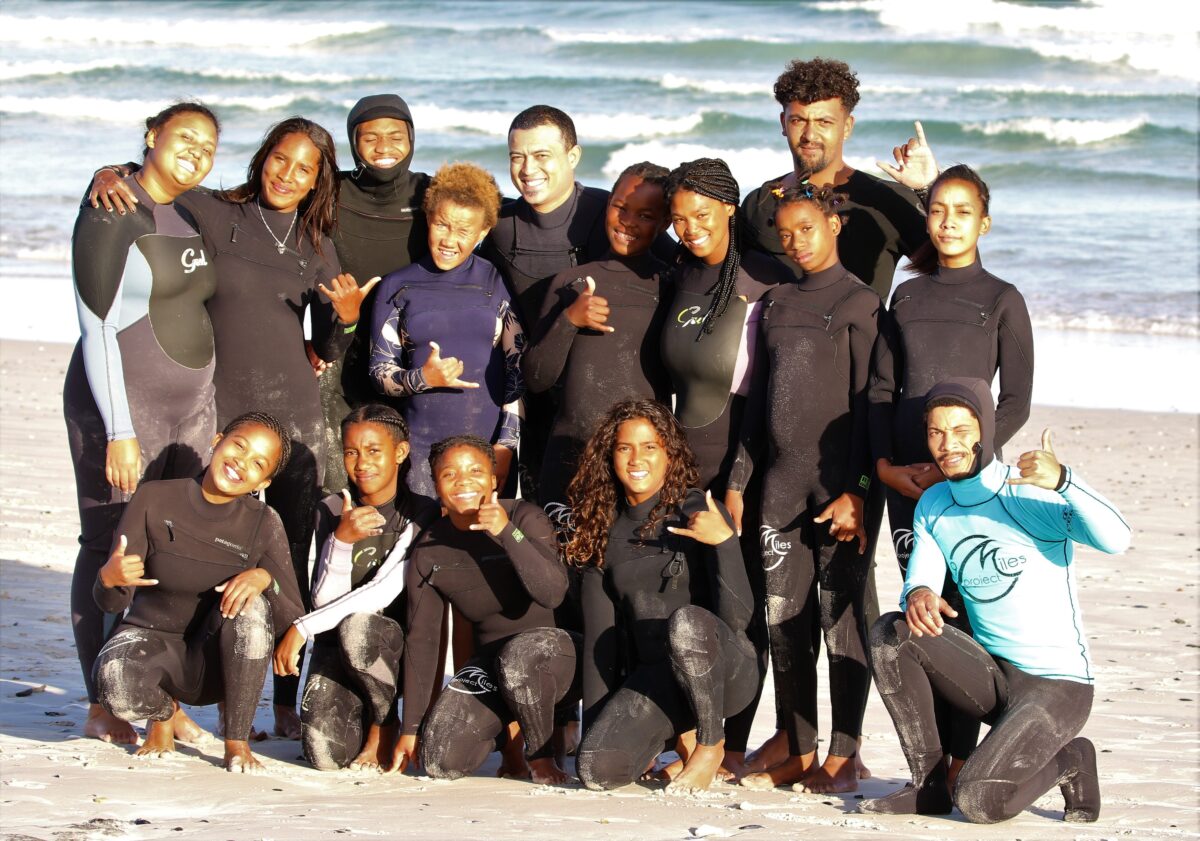 A group of people in wetsuits pose for a photo on a beach