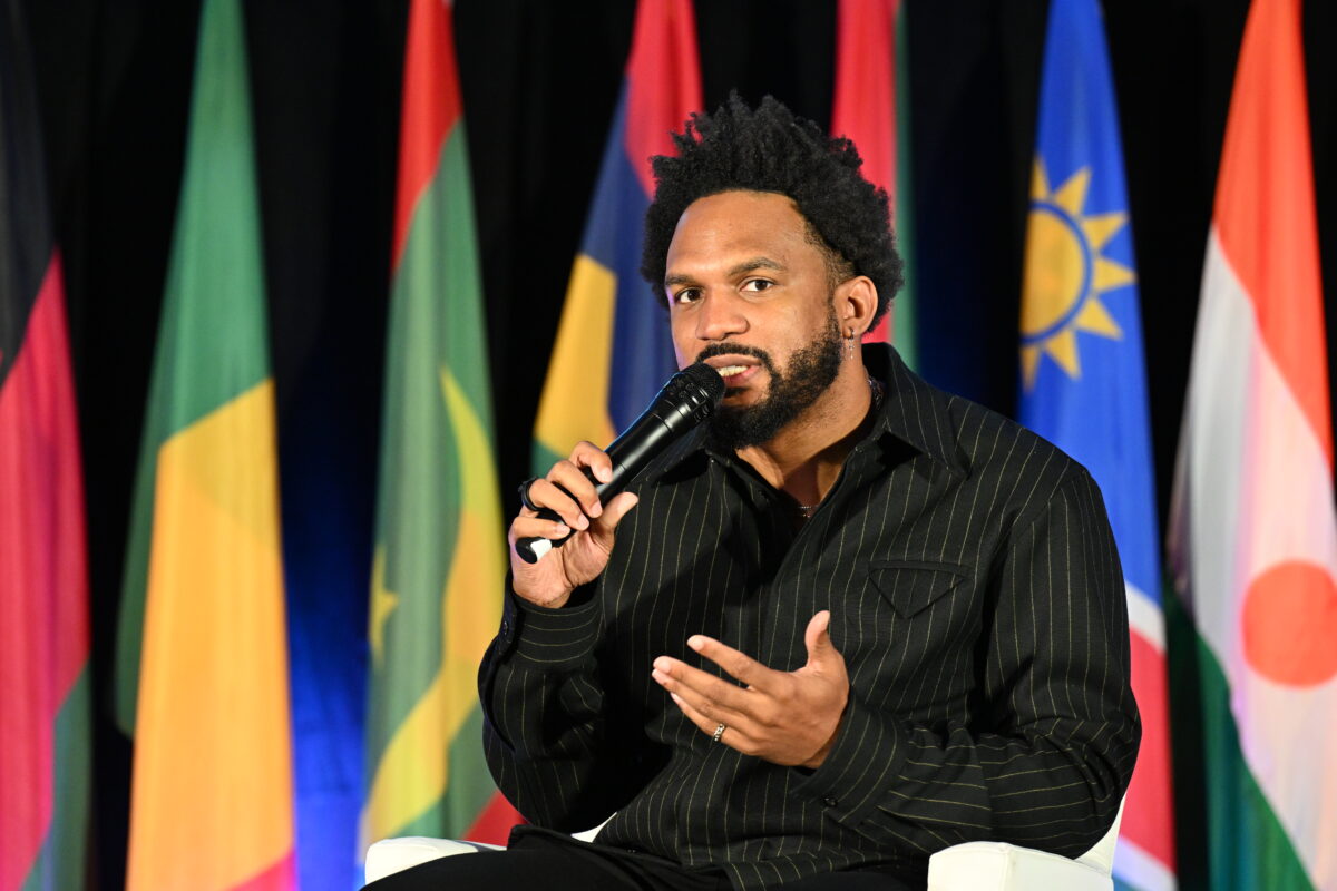 A black man speaks into a microphone and gestures with his hands