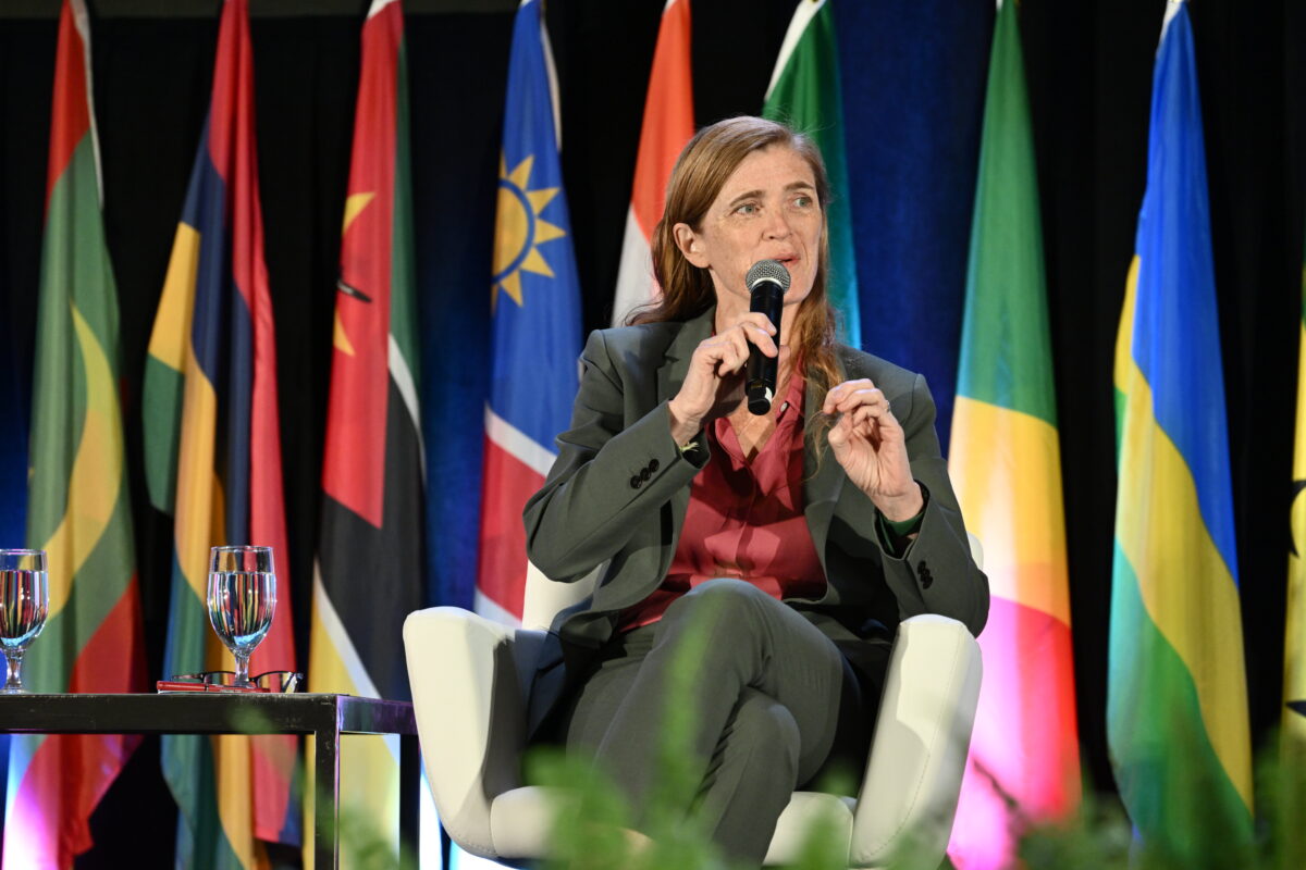 A woman in a suit sits in a chair and speaks into a microphone