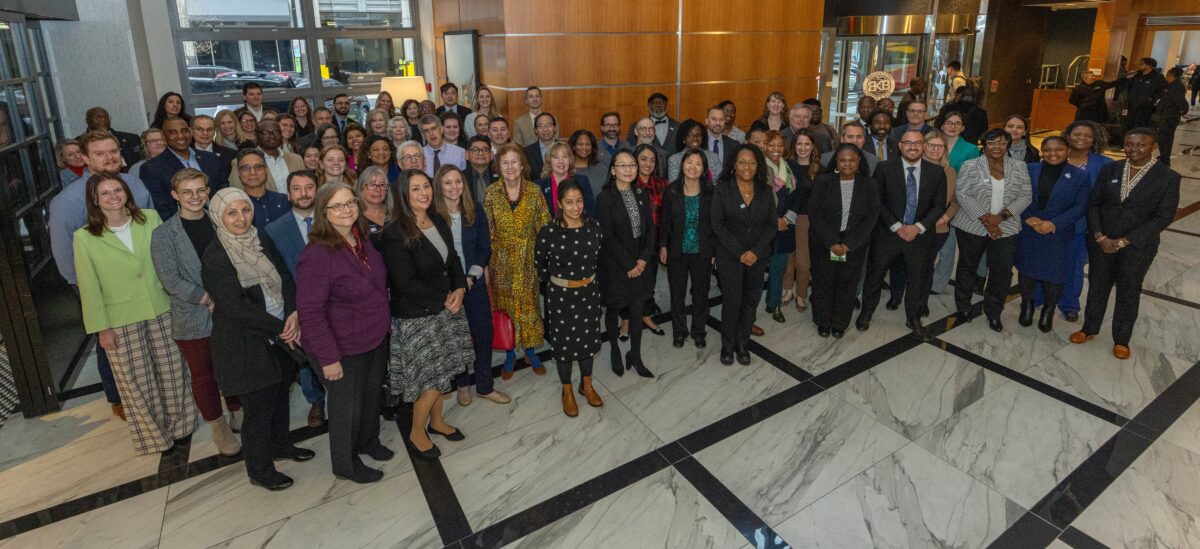 A large group of people smile at the camera for a photo posed in an atrium