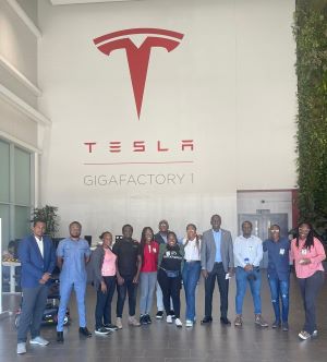 A group of people stand below a sign on a wall reading Tesla Gigafactory 1