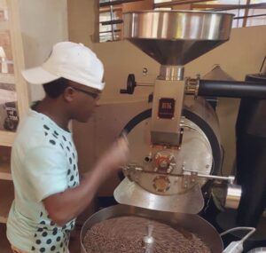 Man monitors coffee beans in a cylindrical metal roasting machine