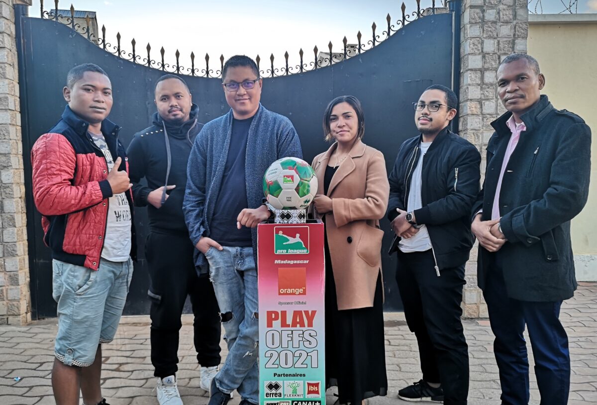 A group of people in business attire stand around a soccer trophy