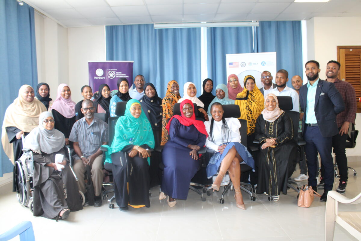 Group of seated and standing people, many who are women in headscarves and one in a wheelchair, pose and smile for the camera